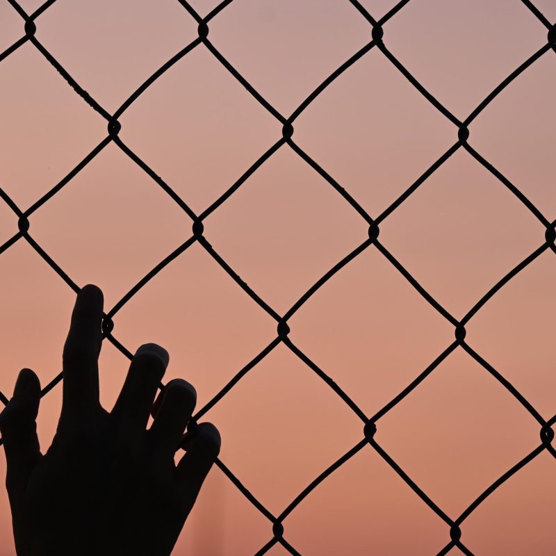 silhouette one human hand in fence, sunset background and copy space, afghanistan conflict concept